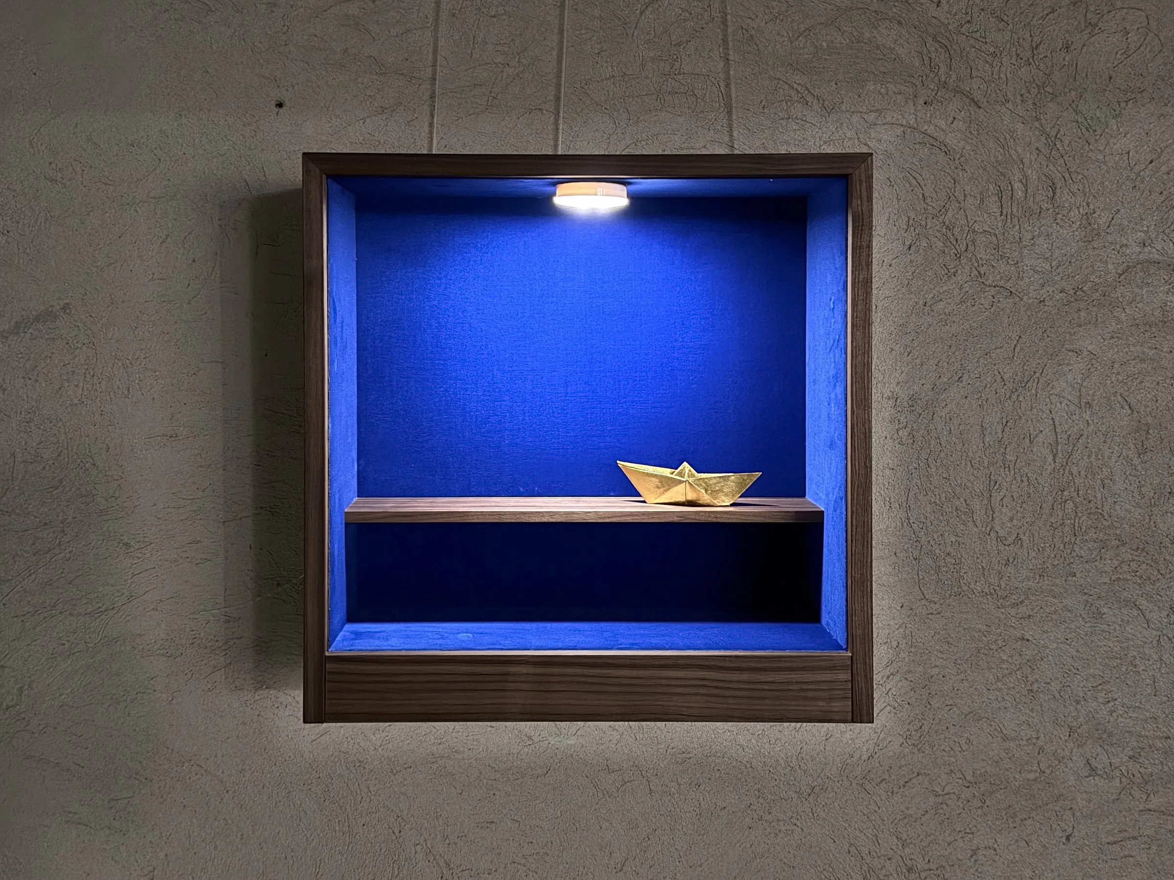 Vitrine mit goldenem Papierschiffchen an der Betonwand