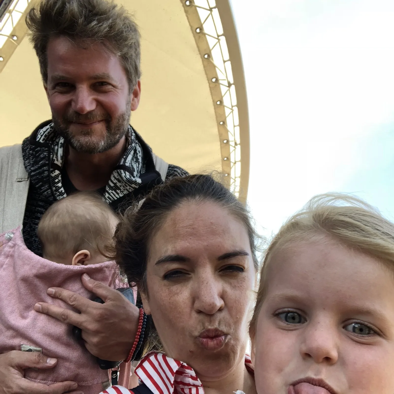 Philipp mit einem Baby auf dem Arm, davor eine Frau und ein Mädchen mit herausgestreckter Zunge, Selfie