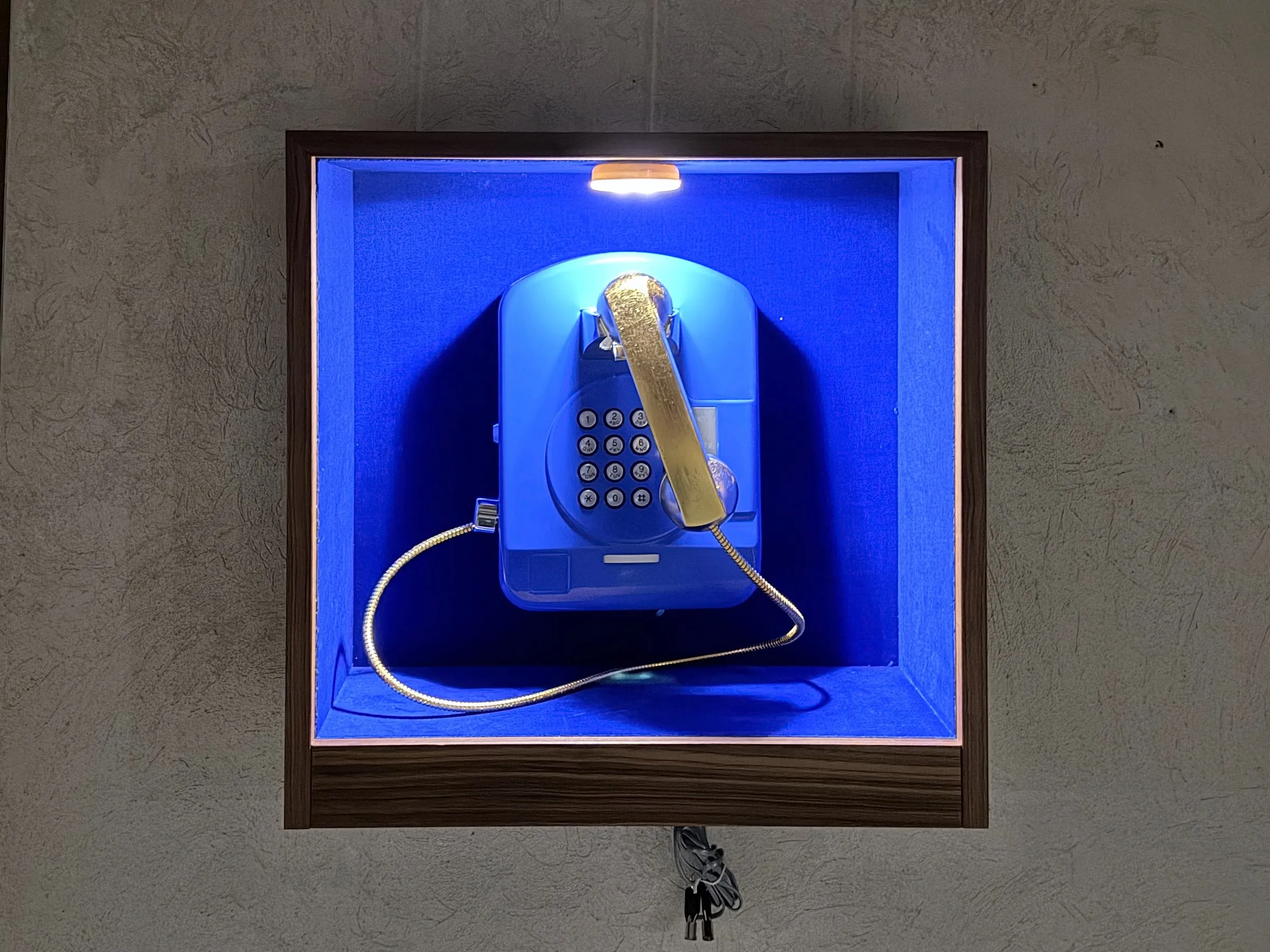 Vitrine mit blauem Wandtelefon an der Betonwand