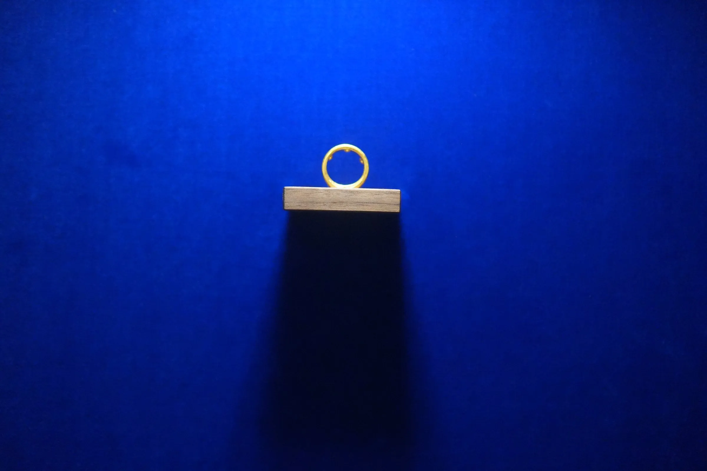 Goldener Ring auf einem Walnuss-Brettchen vor blauem Samt