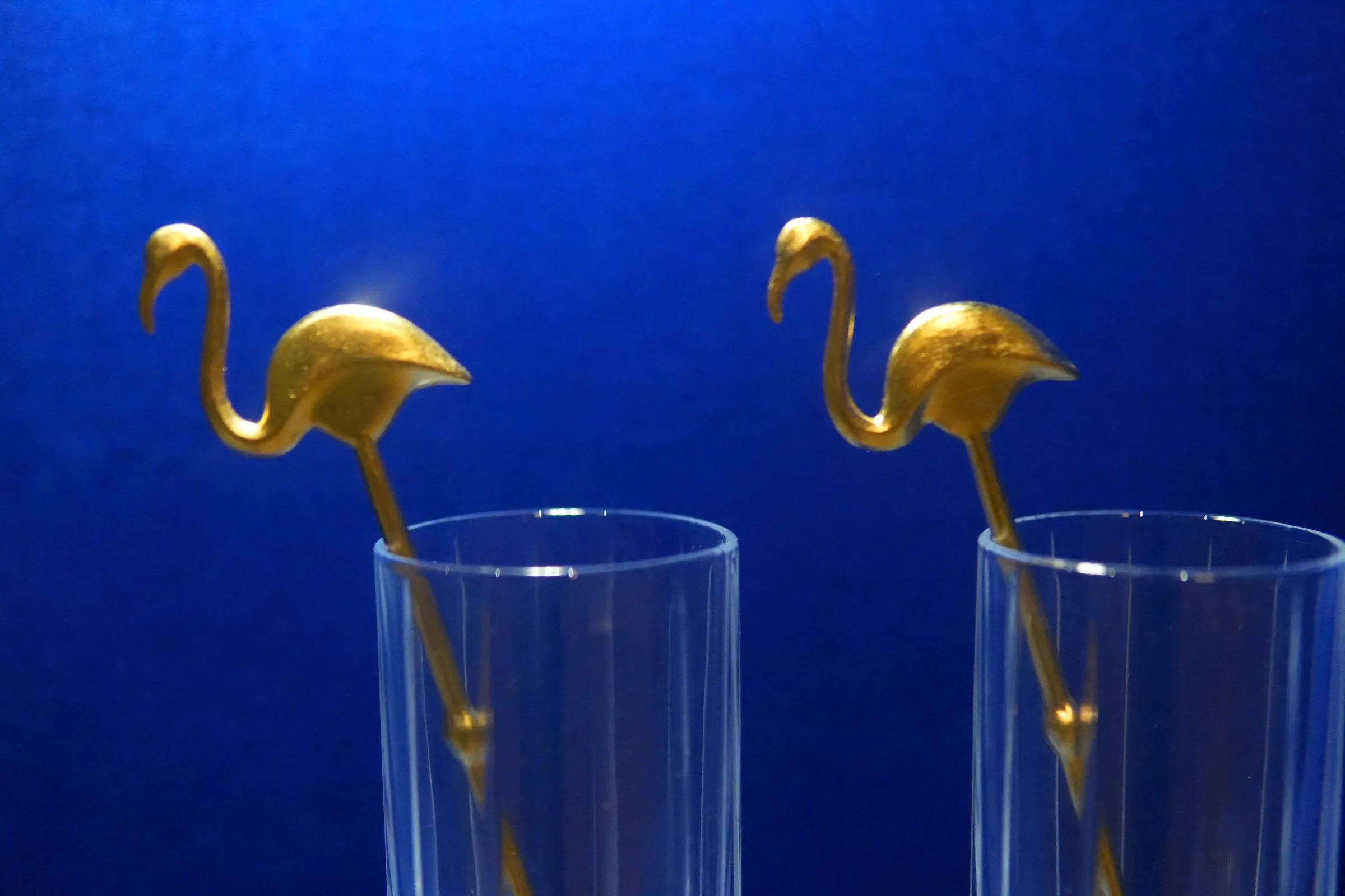 Goldene Flamingo-Rührer in zwei Gläsern vor blauem Samt